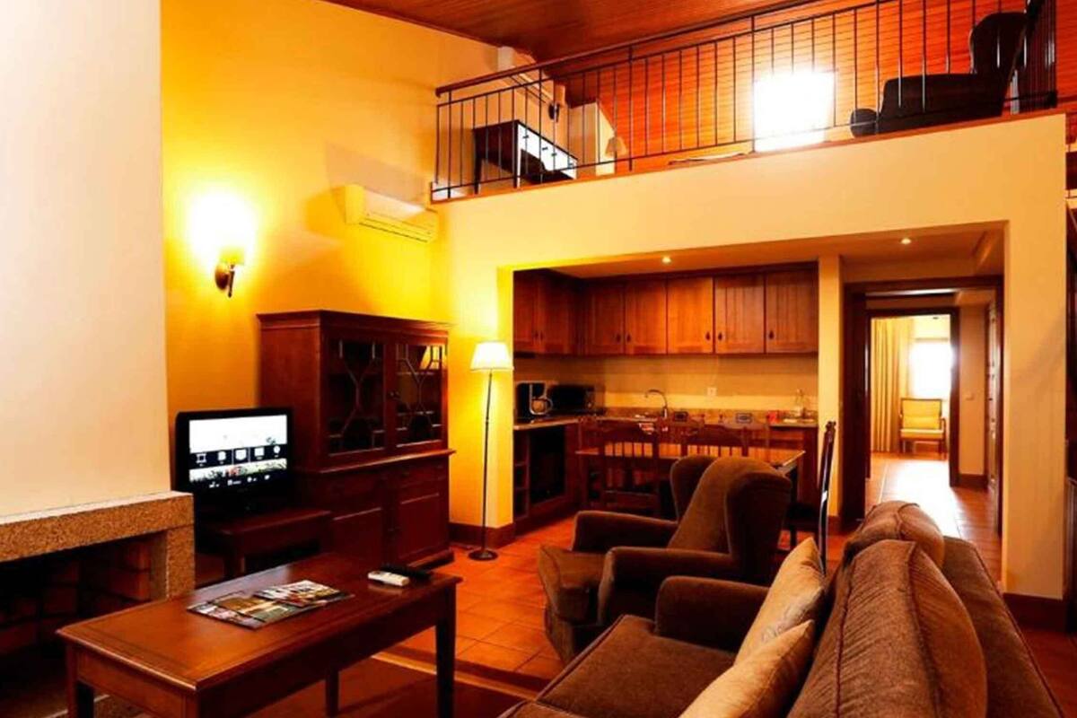 A living room with a fireplace, a television, and a kitchen area visible through an open door.