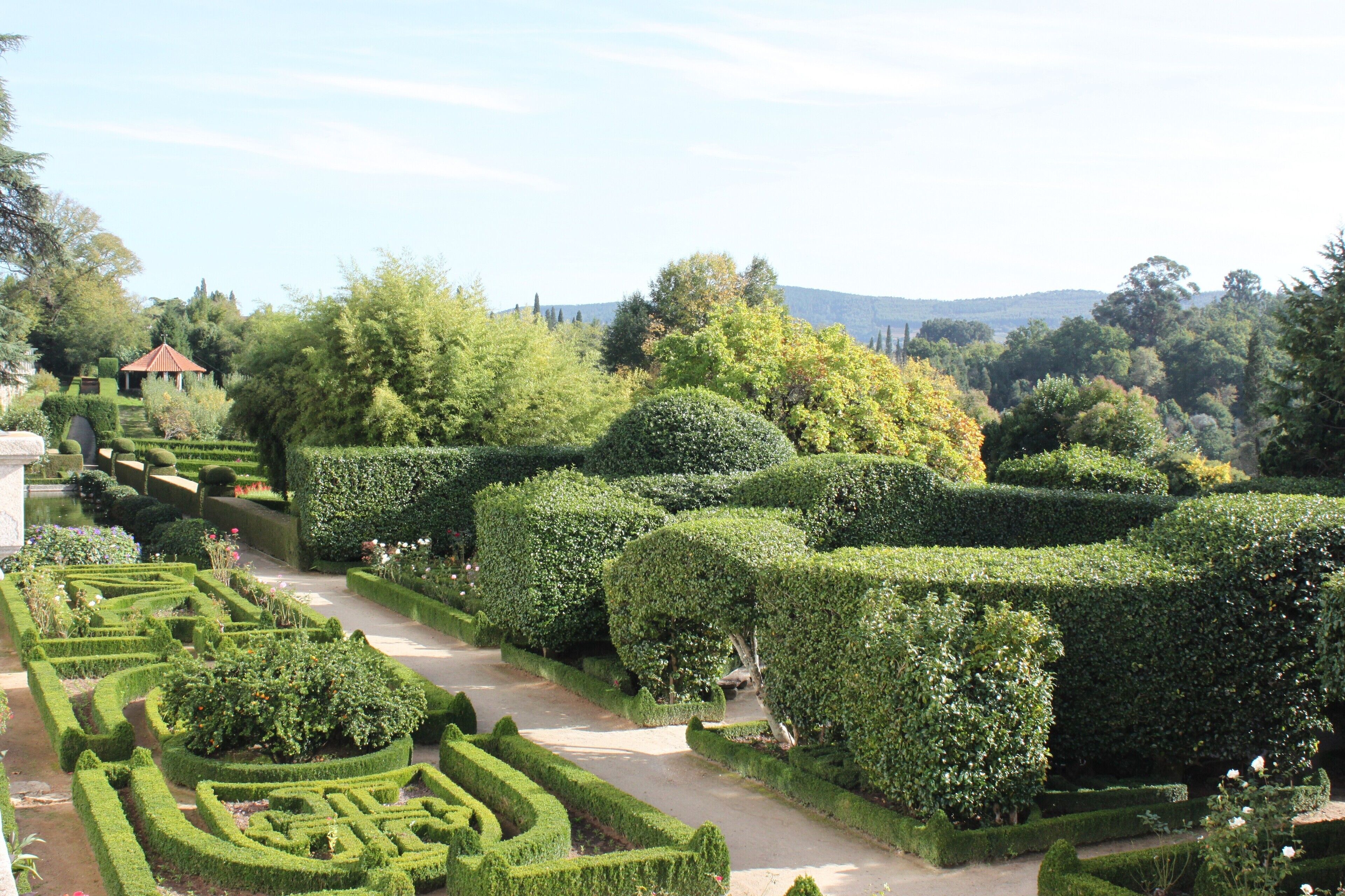 A formal garden with geometric hedges and a small pavilion.