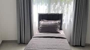 Ein Einzelbett mit Kopfteil, graue Vorhänge und Blick auf Grünflächen.