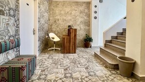 Ein Korridor mit gemusterten Bodenfliesen, einer Treppe, einem Empfangstresen und einer Sitzecke mit einem gemusterten Sofa.