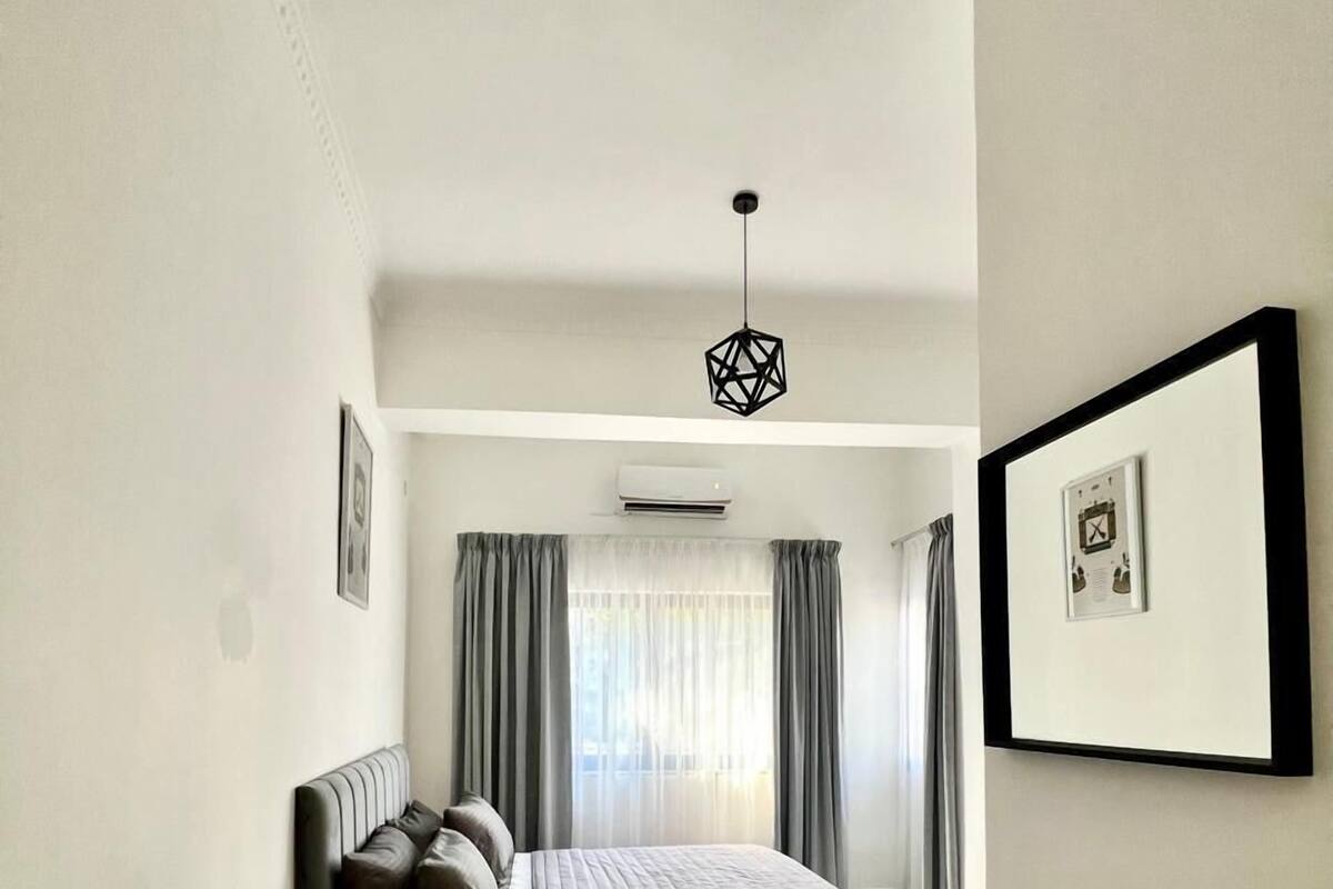 A modern bedroom with a bed, a wooden nightstand, a hanging light fixture, and a framed picture on the wall.