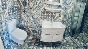 Ein Badezimmer mit Toilette und Waschbecken, beide weiß, mit gemusterten Fliesen an Wänden und Boden.