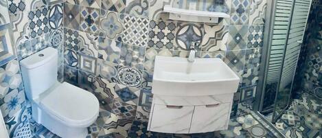 Un baño con inodoro y lavamanos, ambos blancos, con azulejos estampados en paredes y suelo.