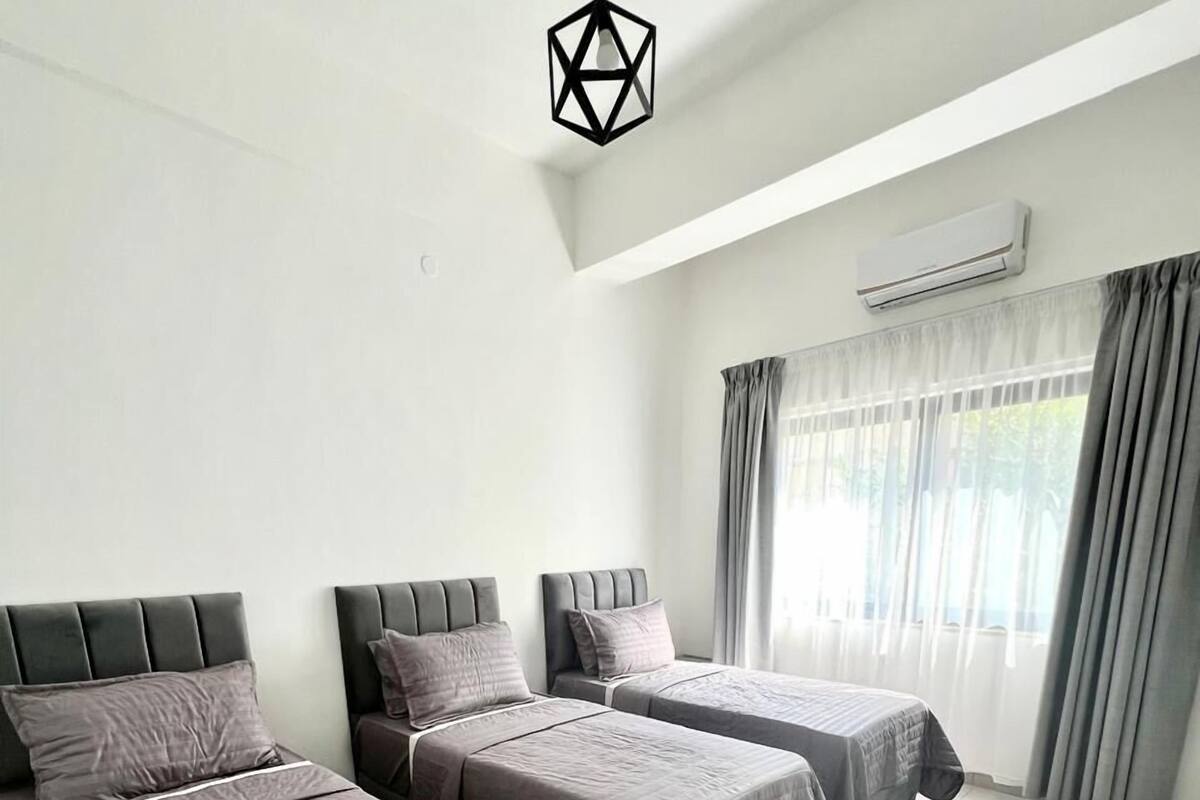 A hotel room with three beds, a modern pendant light, an air conditioning unit, and a large window with curtains.