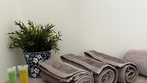 Ein Holzboden mit aufgerollten Handtüchern, einer Topfpflanze und zwei Kosmetikflaschen.