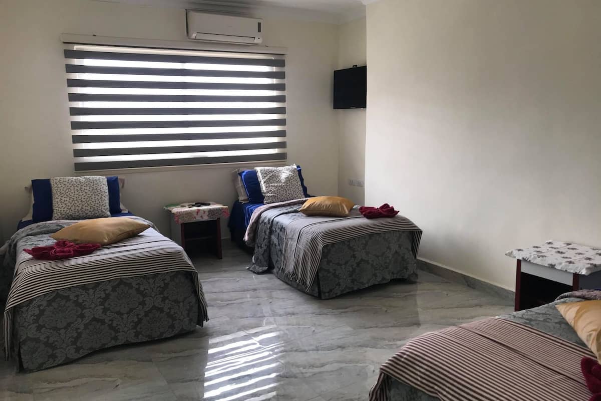 A room with two beds, a small table, and a TV mounted on the wall.
