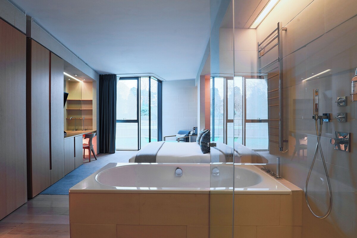 Un baño moderno con una bañera grande, ducha y un área de estar con vistas, todo envuelto en vidrio.