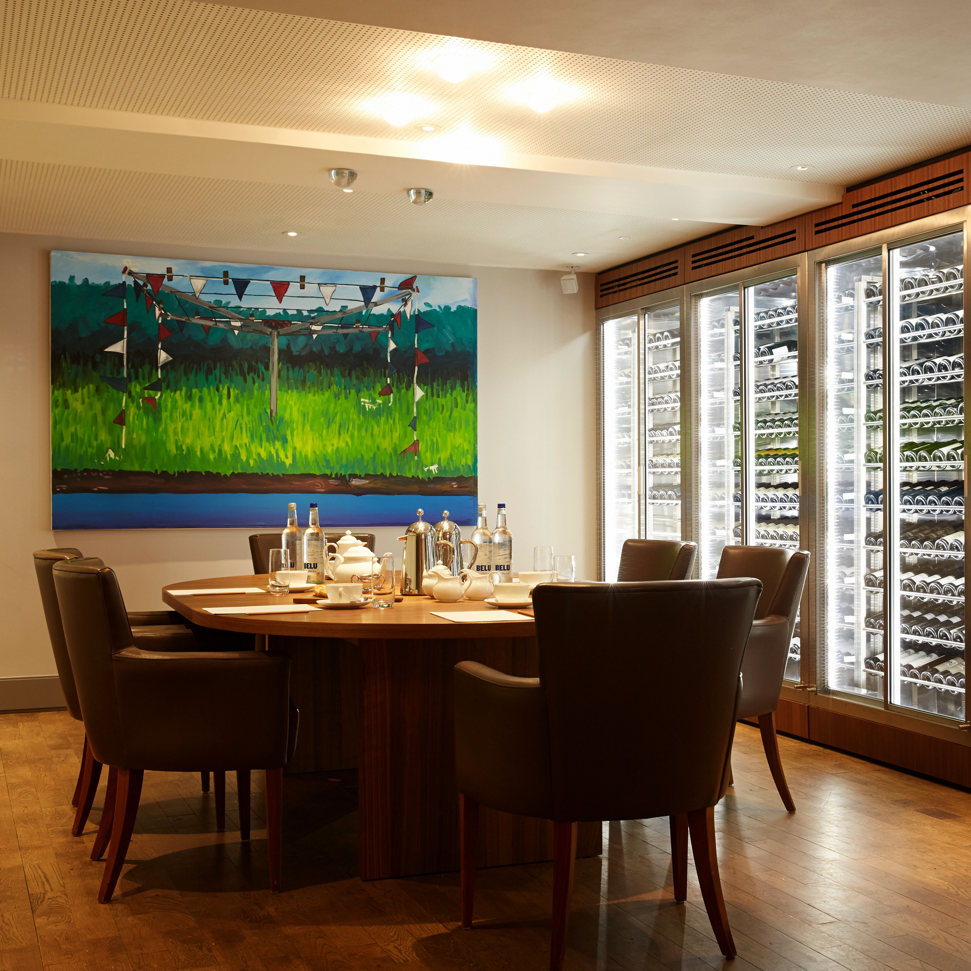 A dining area with a round table, chairs, and a painting on the wall.
