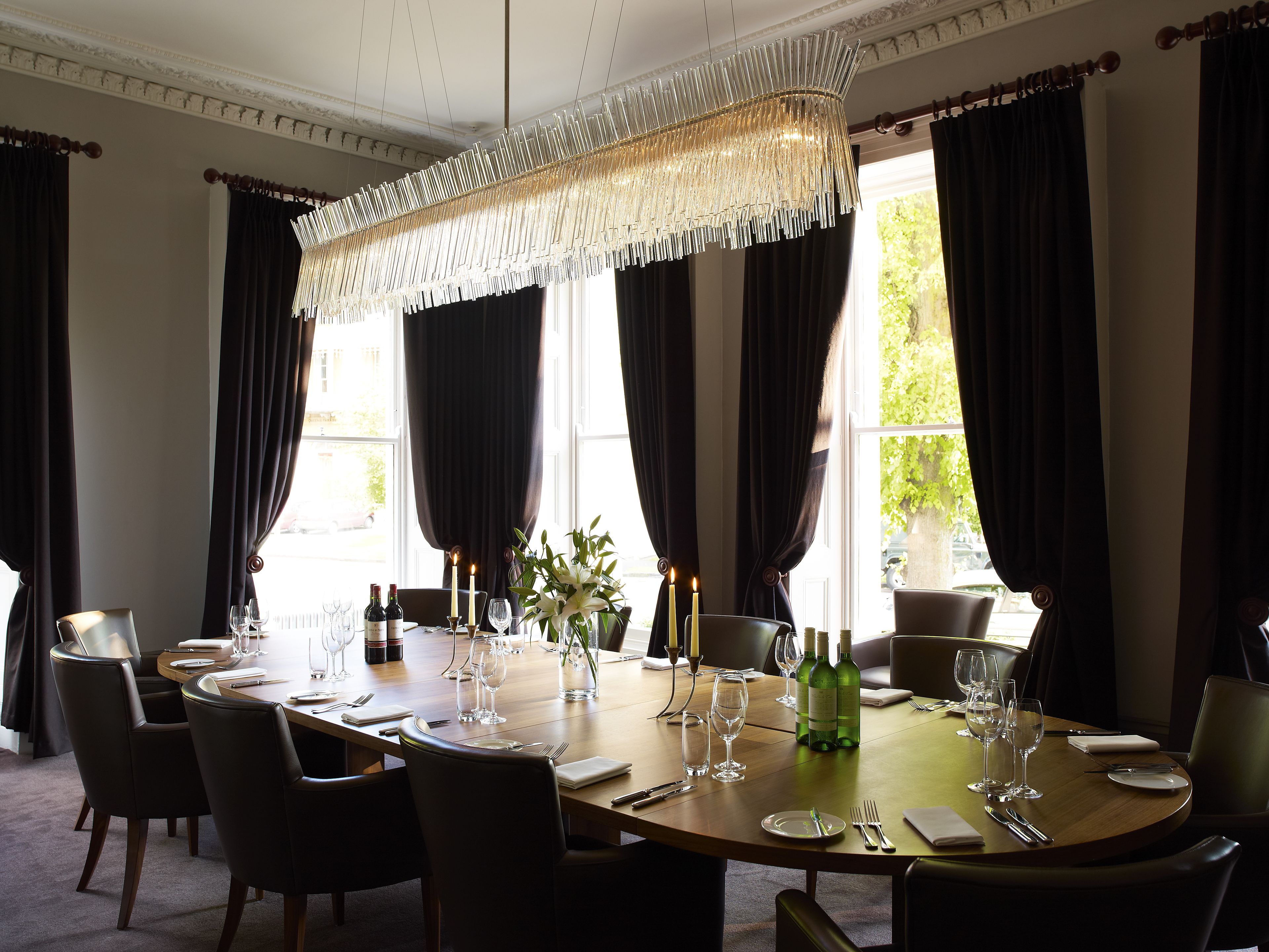 Une salle à manger avec une table ronde dressée pour six personnes, agrémentée d’un lustre, de bougies et de bouteilles de vin.