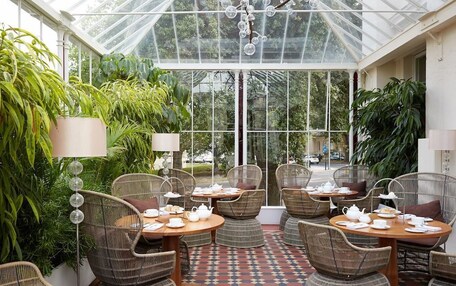 A conservatory with wicker furniture, glass ceiling, and lush greenery.