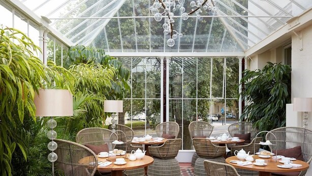 A conservatory with wicker furniture, glass ceiling, and lush greenery. - Malmaison Cheltenham (Cheltenham)