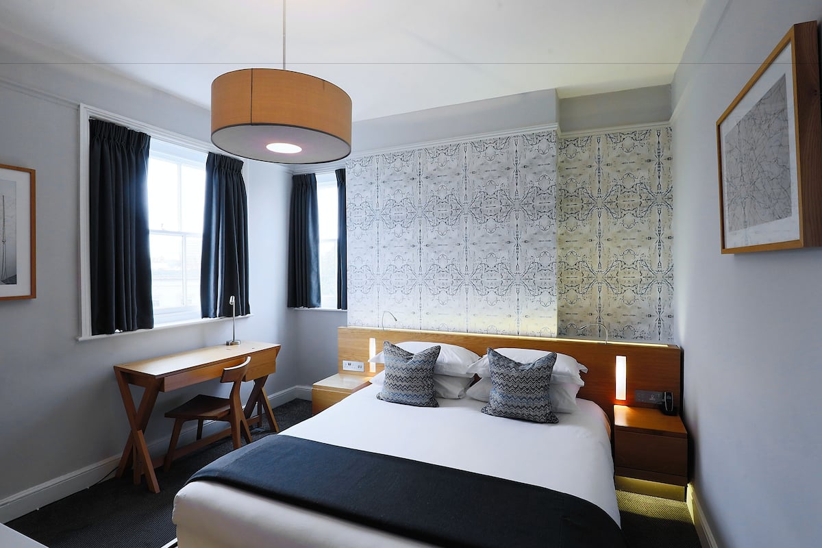 A hotel room with a bed, desk, chair, and a large window with curtains.