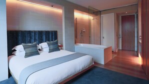 A modern bedroom with a large bed, a built-in bench, a shower, and a separate bathroom. - Malmaison Cheltenham (Cheltenham)