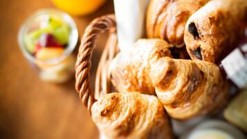 A basket of croissants and a glass of orange juice on a wooden table.
