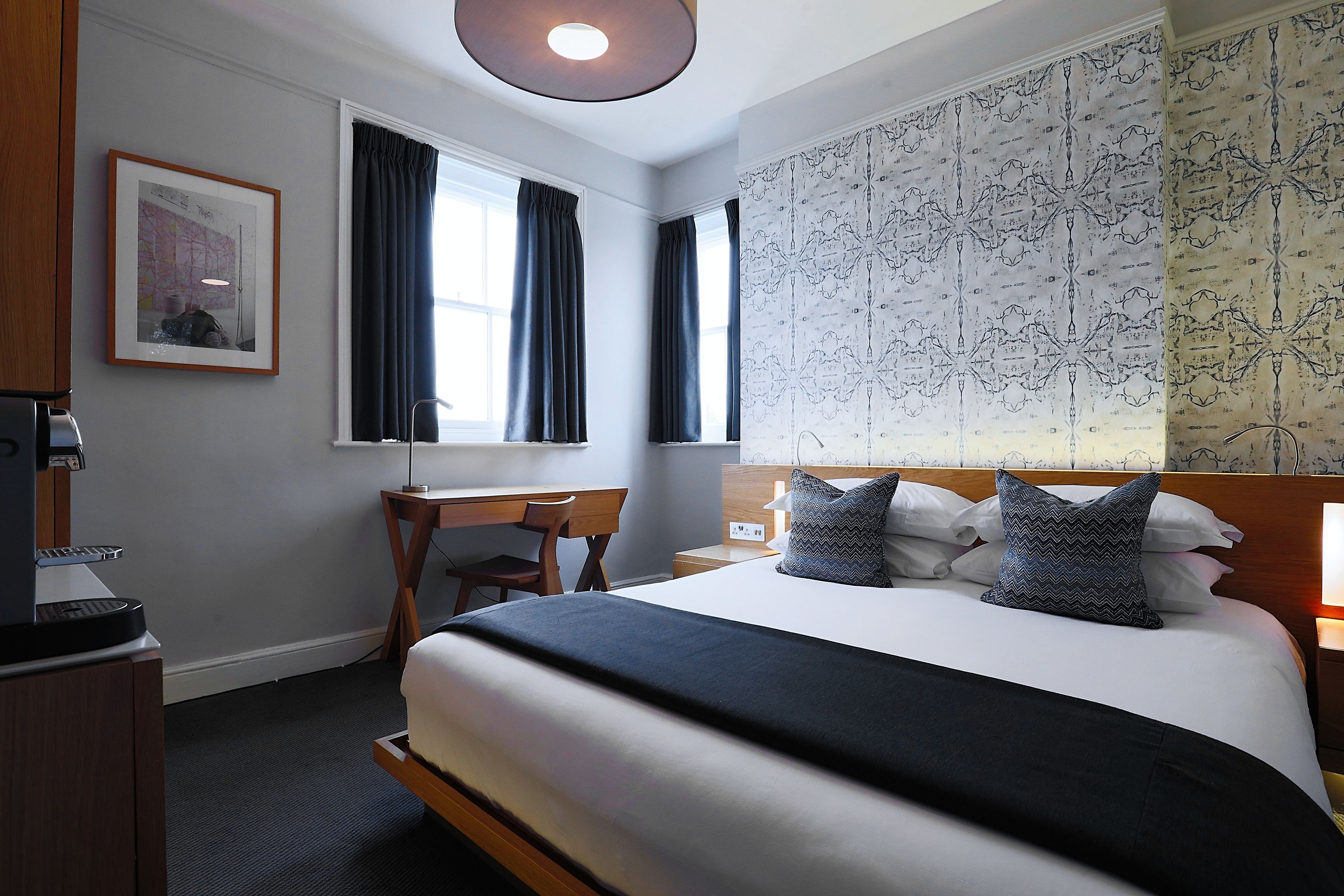 A hotel room with a bed, desk, chair, and a large window with curtains.