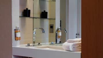 A modern bathroom with a glass shelf holding toiletries, a white sink with a chrome faucet, and a towel stacked on the counter.