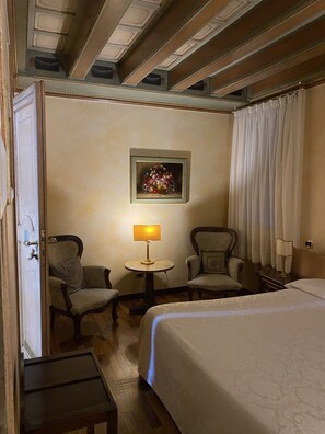 A hotel room with a bed, two armchairs, a small table with a lamp, and a painting on the wall. - Hotel Residence Il Chiostro (Oppeano)