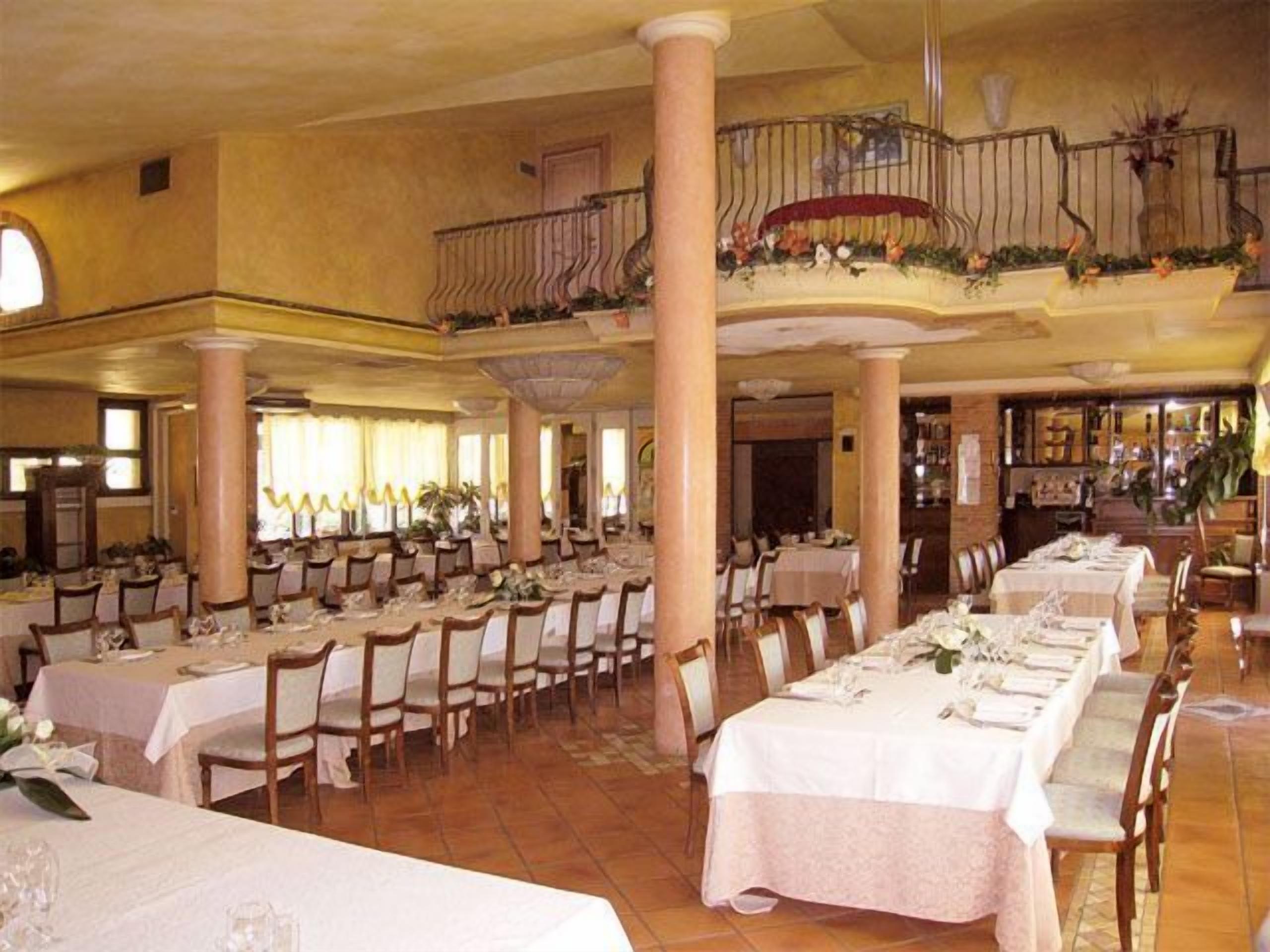 A large banquet hall with multiple long tables set for dining, high ceilings, and a balcony with railings.