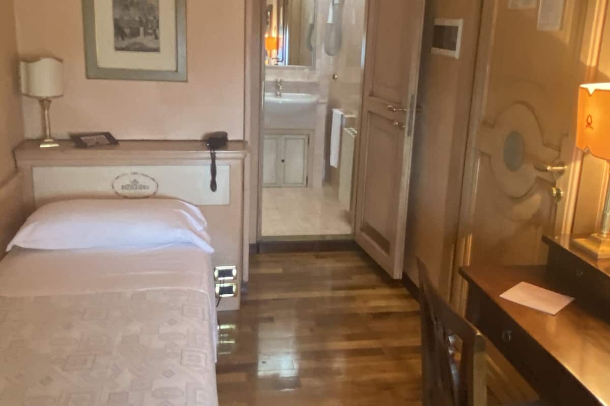 A hotel room with a bed, bedside table, chair, and a bathroom visible through an open door.