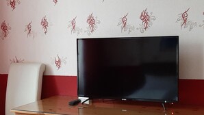 Un televisor sobre un escritorio de madera con cajones, frente a una pared con papel tapiz de estampado rojo y blanco.