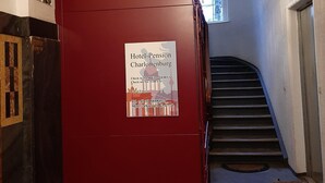 Pared roja con un cartel de Hotel Pension Charlottenburg, que muestra horarios de entrada y números de contacto.