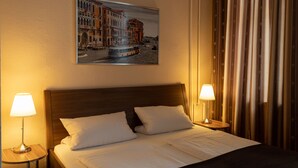 Una habitación de hotel con una cama, dos lámparas de noche, un cuadro de un paisaje urbano y una cortina.