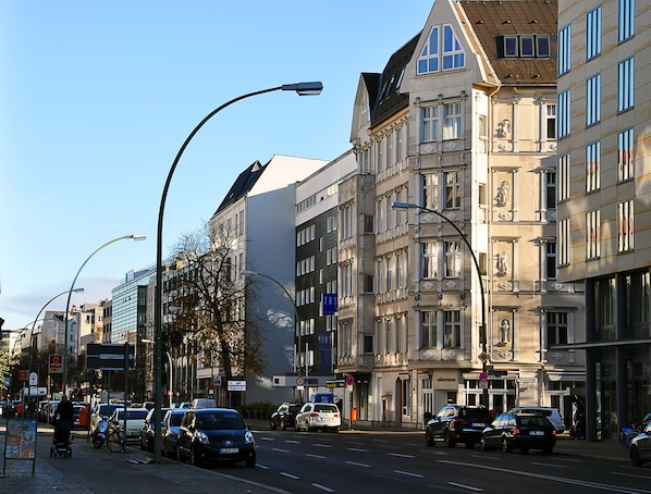 Vista de una calle con edificios históricos, coches aparcados y un peatón.