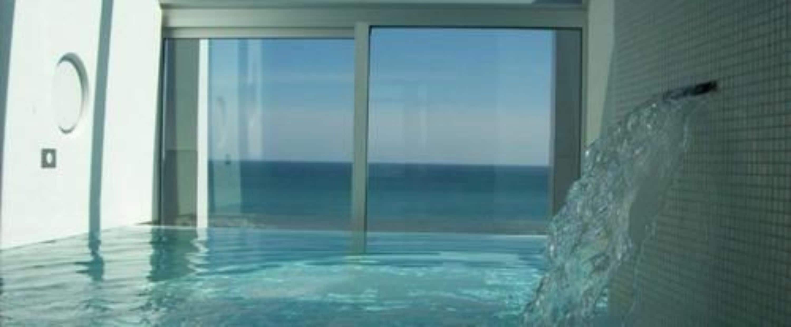 A modern indoor swimming pool with clear glass walls and a view of the ocean.