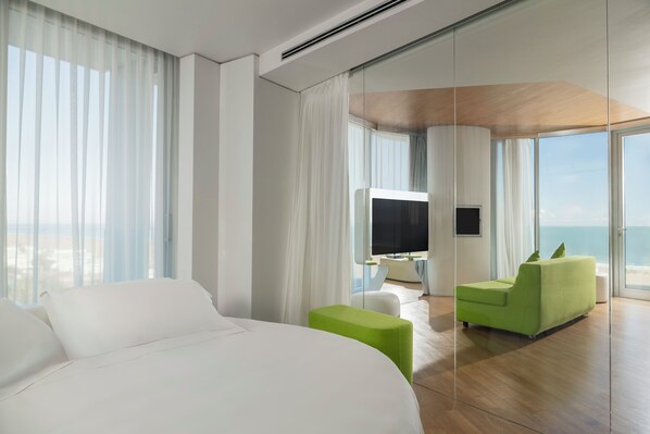 A modern hotel room with a large bed, a green sofa, a TV, and a view of the ocean.