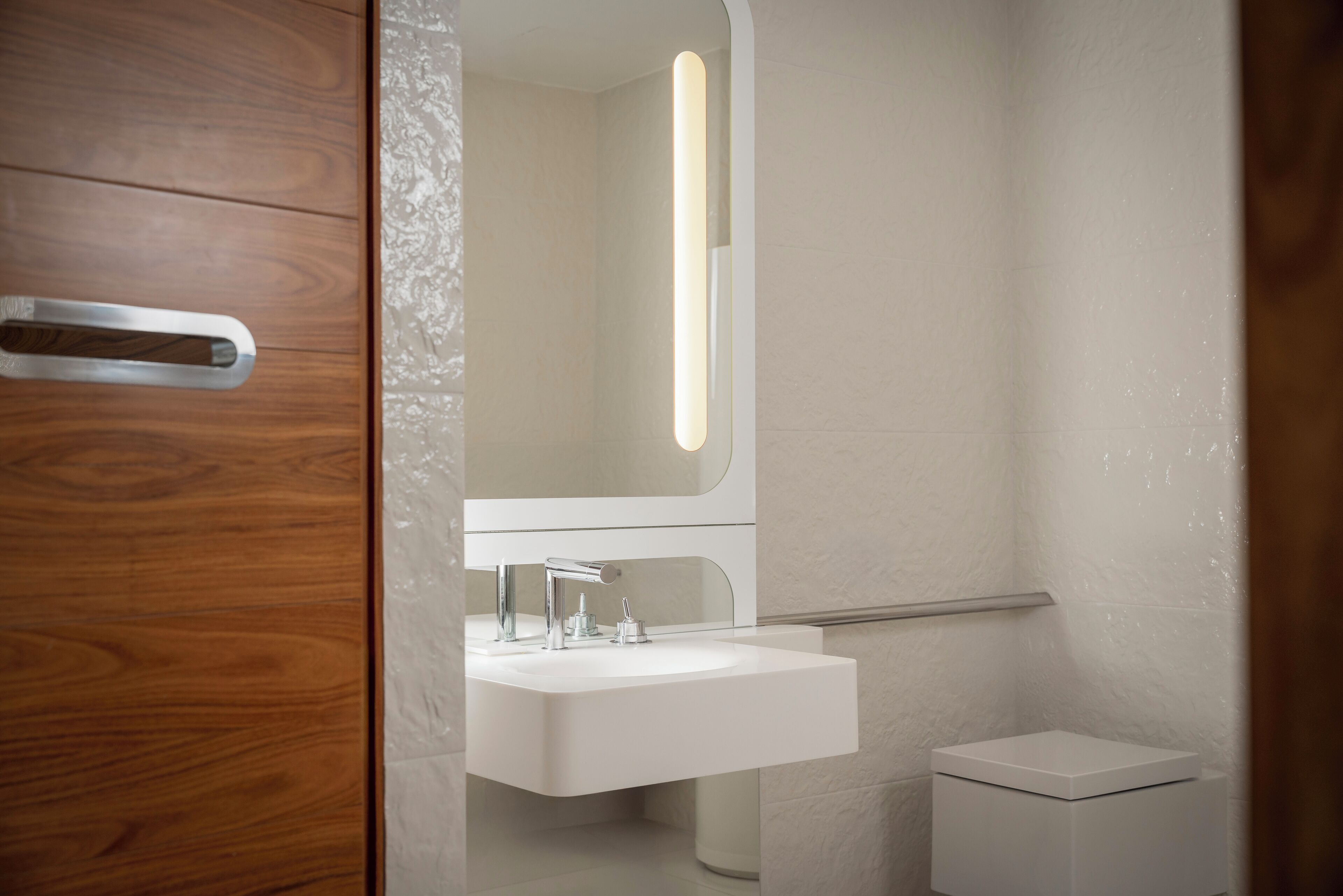 Ein modernes Badezimmer mit Holztür, Waschbecken in Weiß, Spiegel und Toilette in Weiß.