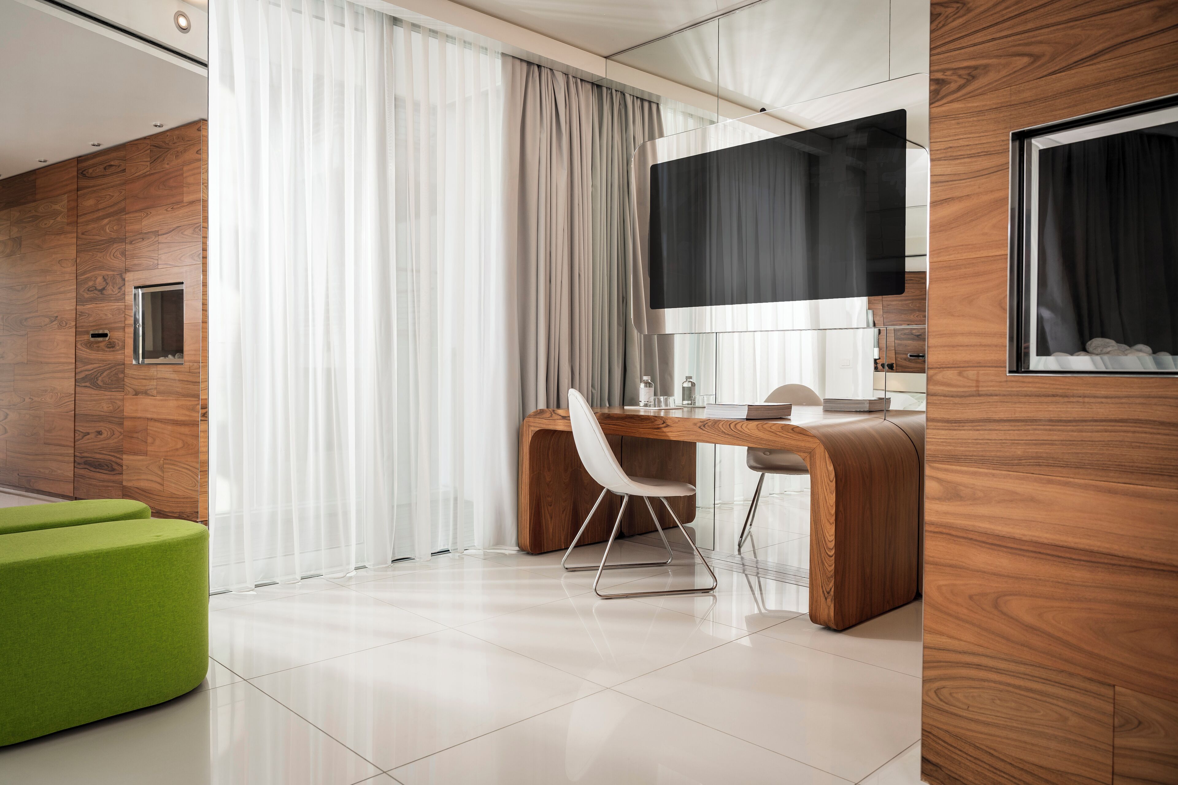 Quarto de hotel moderno com parede de destaque em madeira, uma televisão de tela plana grande, escrivaninha de madeira e um banquinho verde.