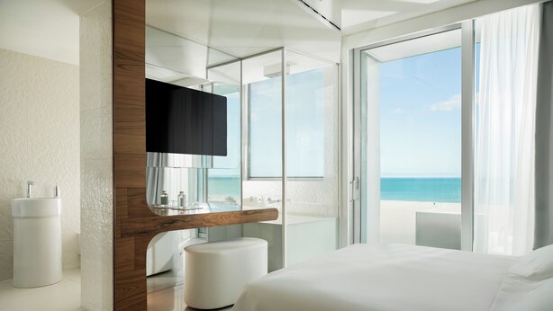 A modern hotel room with a large bed, a bathroom with a bathtub, and a view of the ocean.