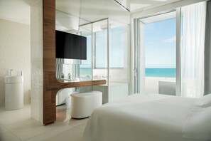 Une chambre d’hôtel moderne avec un grand lit, une salle de bain avec baignoire et vue sur l’océan.