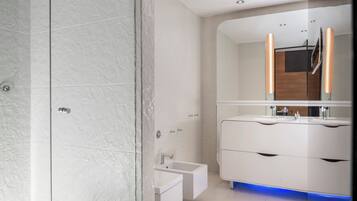 Un baño moderno con pared de ducha de mármol, lavabo empotrado con espejo y tocador con iluminación azul.
