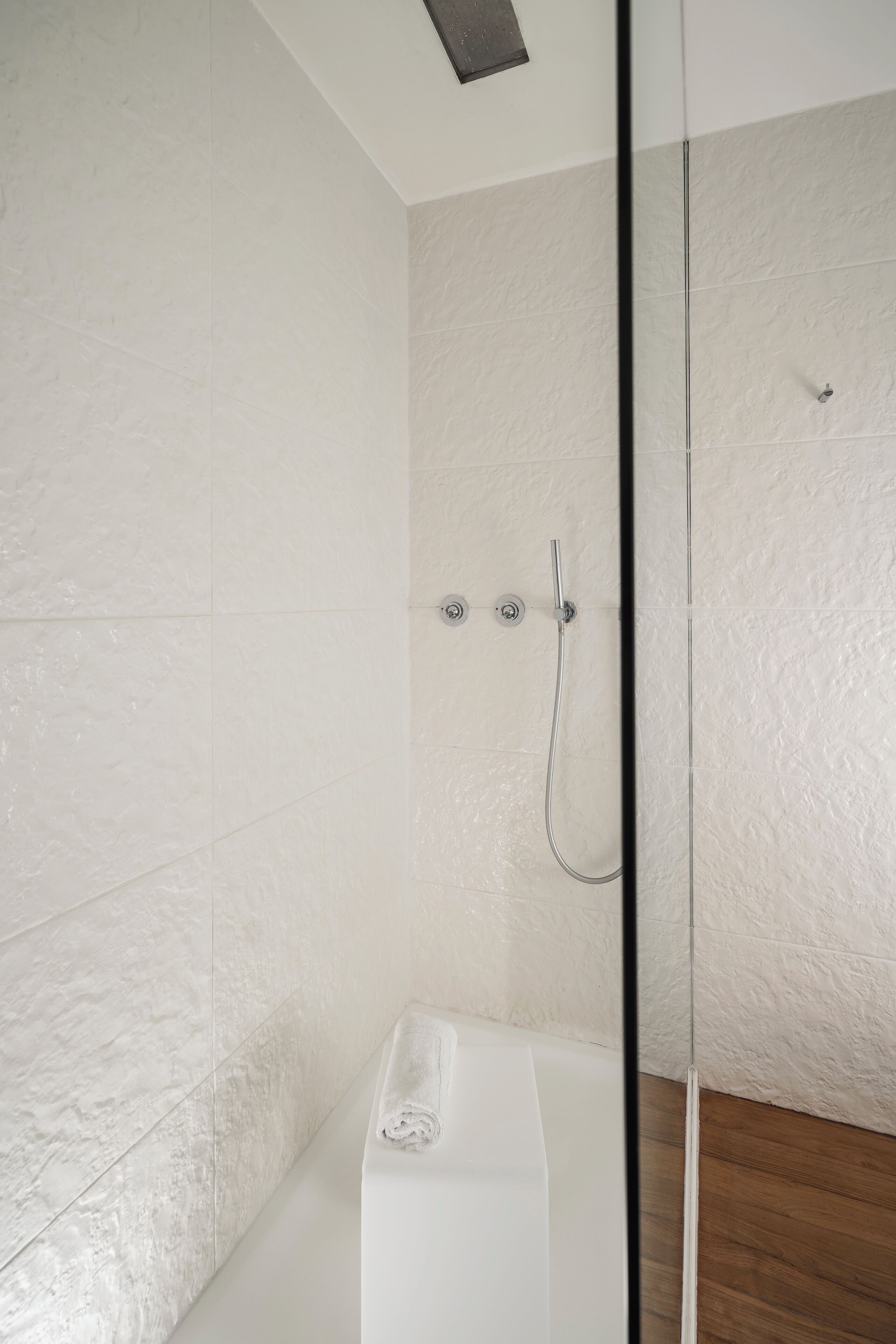 Une salle de bain moderne avec une douche à l’italienne en verre, une baignoire blanche et des murs blancs à texture.