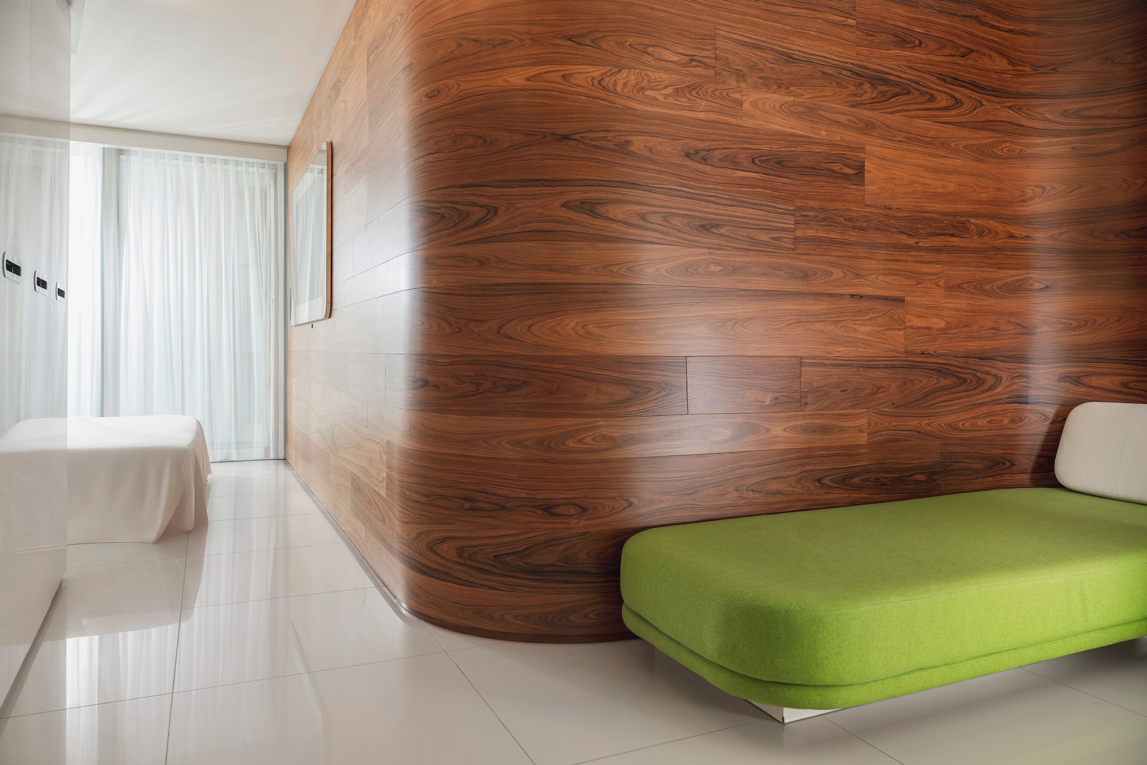 A modern interior with a curved wooden wall, a green cushioned bench, and a white table.