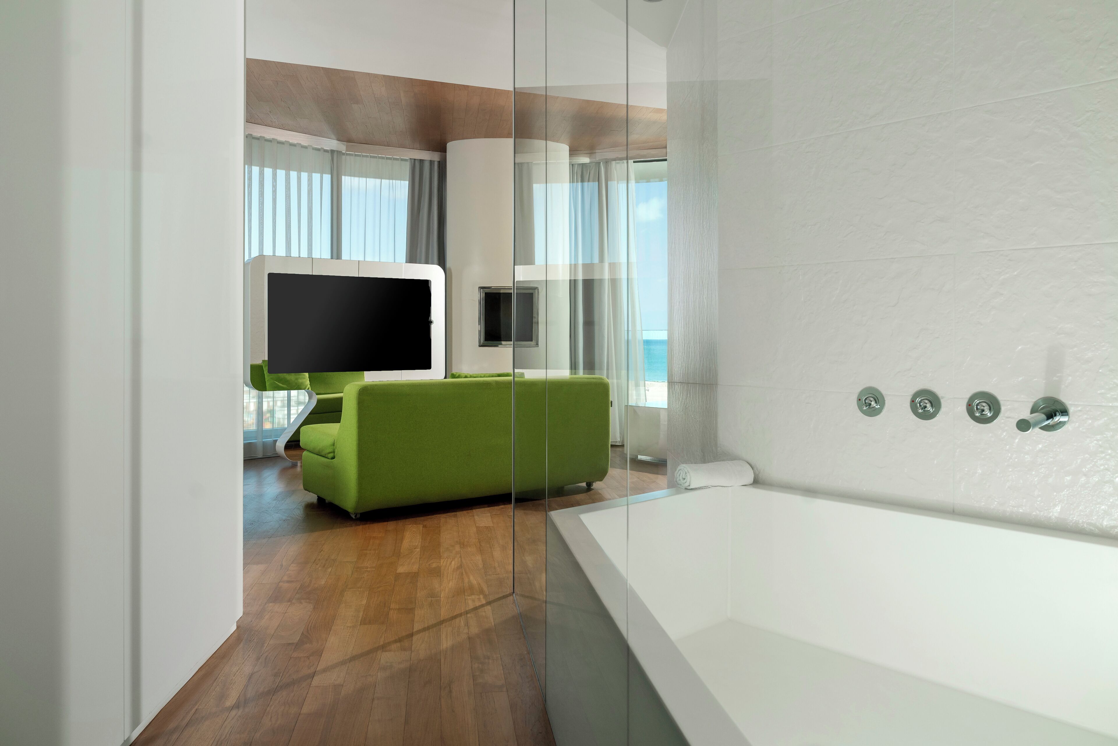 Un baño moderno con una bañera grande, suelo de madera y un sofá verde al fondo.