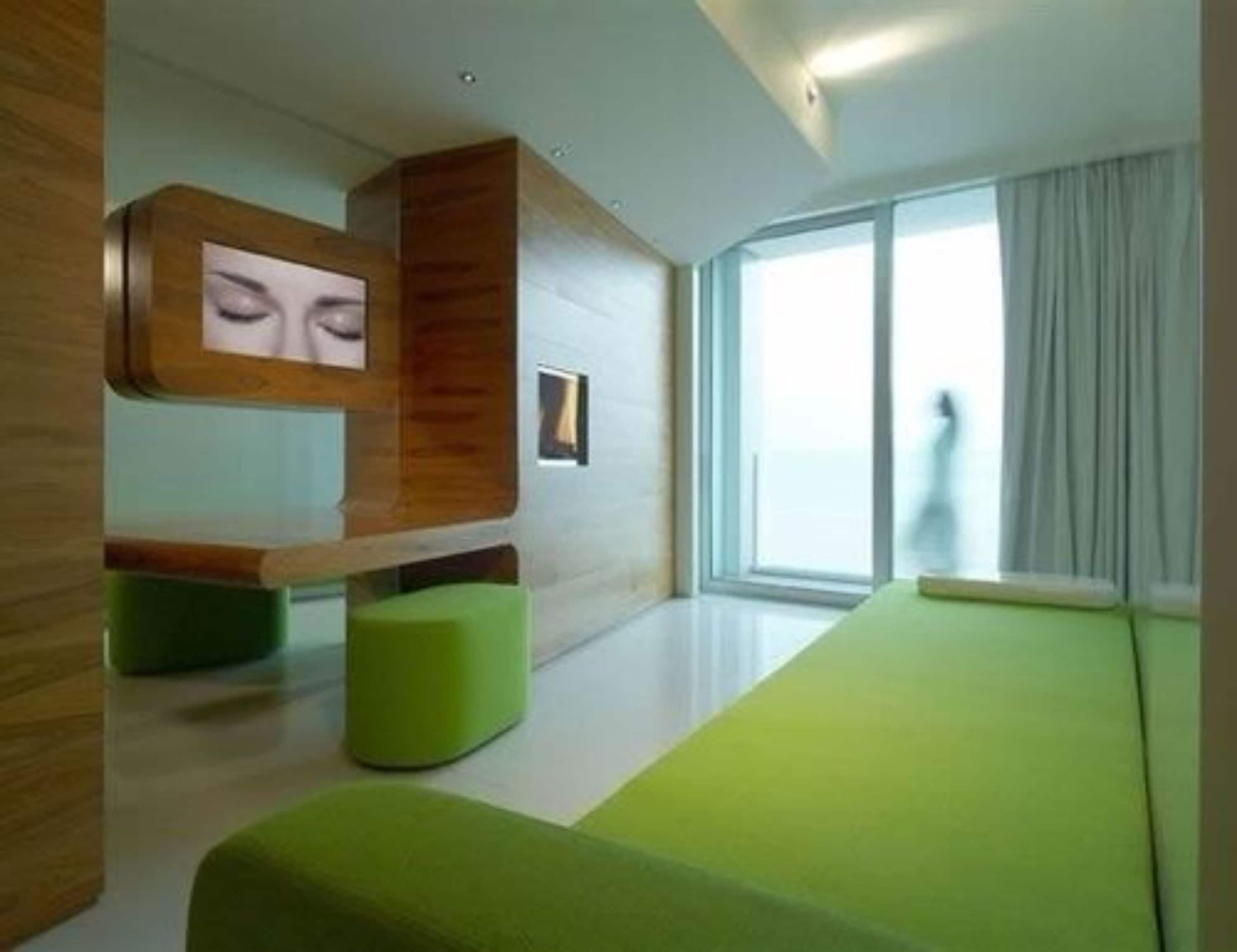Habitació d'hotel moderna amb un sofà verd, detalls de fusta i un gran finestral amb vista.