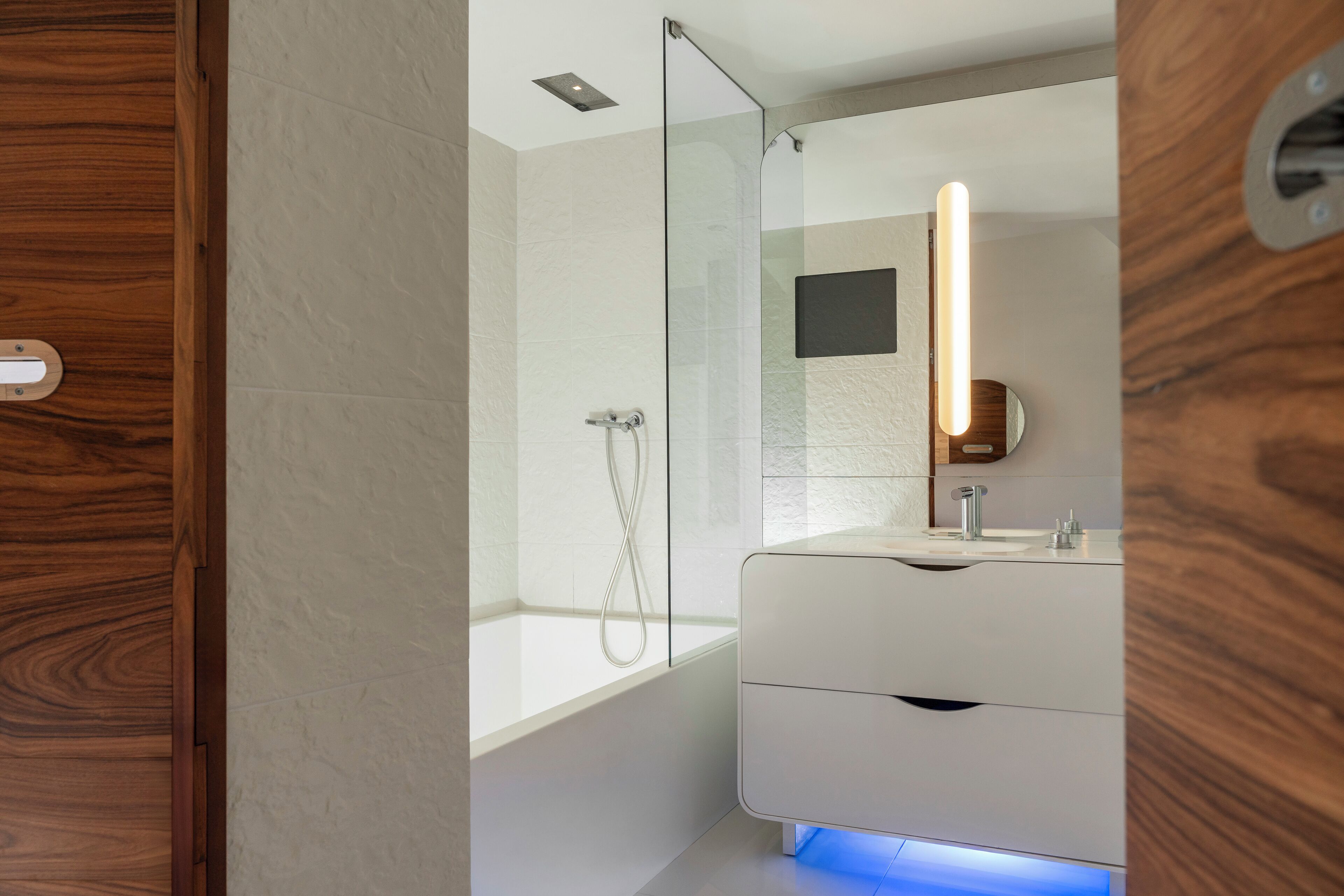 Un bagno moderno con box doccia in vetro, un mobile lavabo bianco con specchio e una luce blu sotto il pensile.