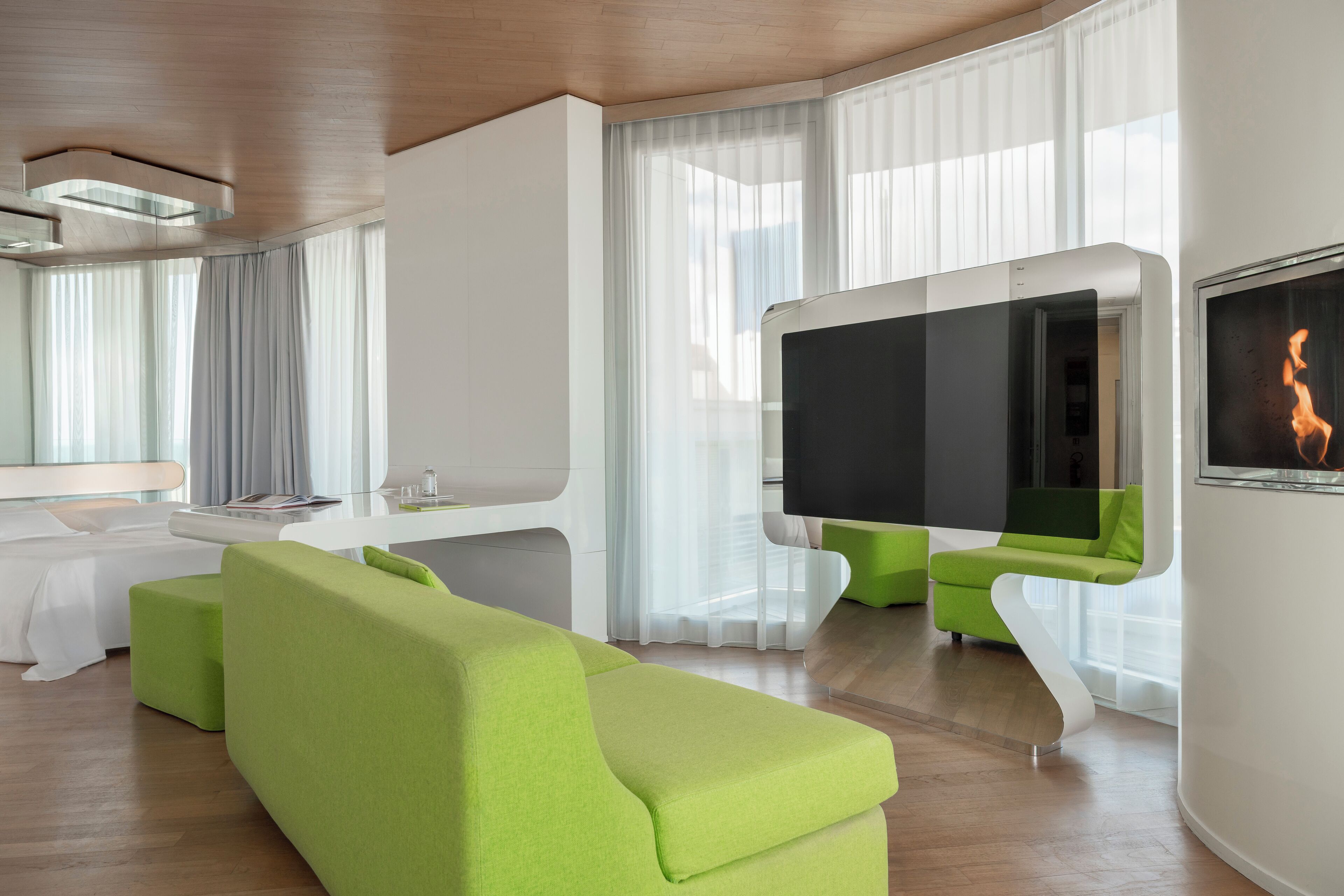 A modern living room with a green sofa, a flat-screen TV, and a dining area with a white table and chairs.