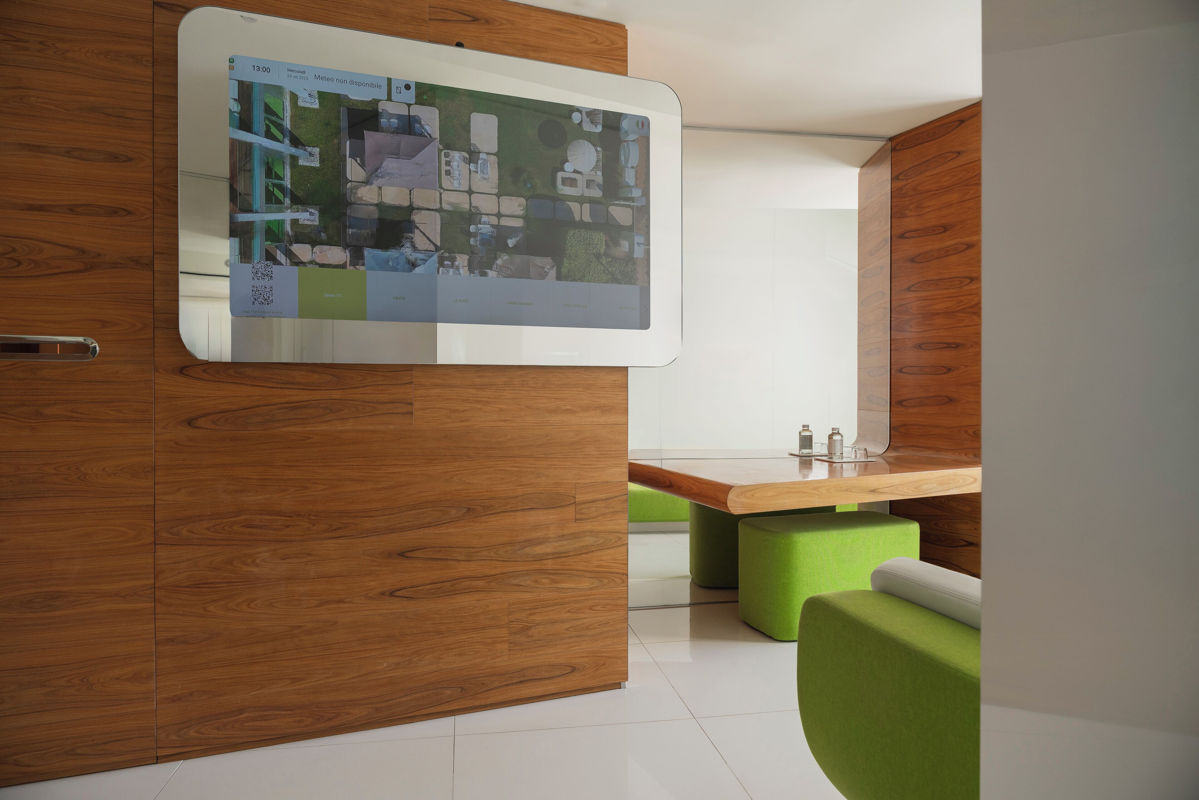Una camera moderna con un divisorio in legno, un display digitale a parete e posti a sedere verdi.