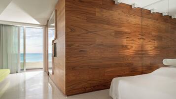A modern bedroom with a large wooden panel wall, a bed, and a view of the beach through a glass door.