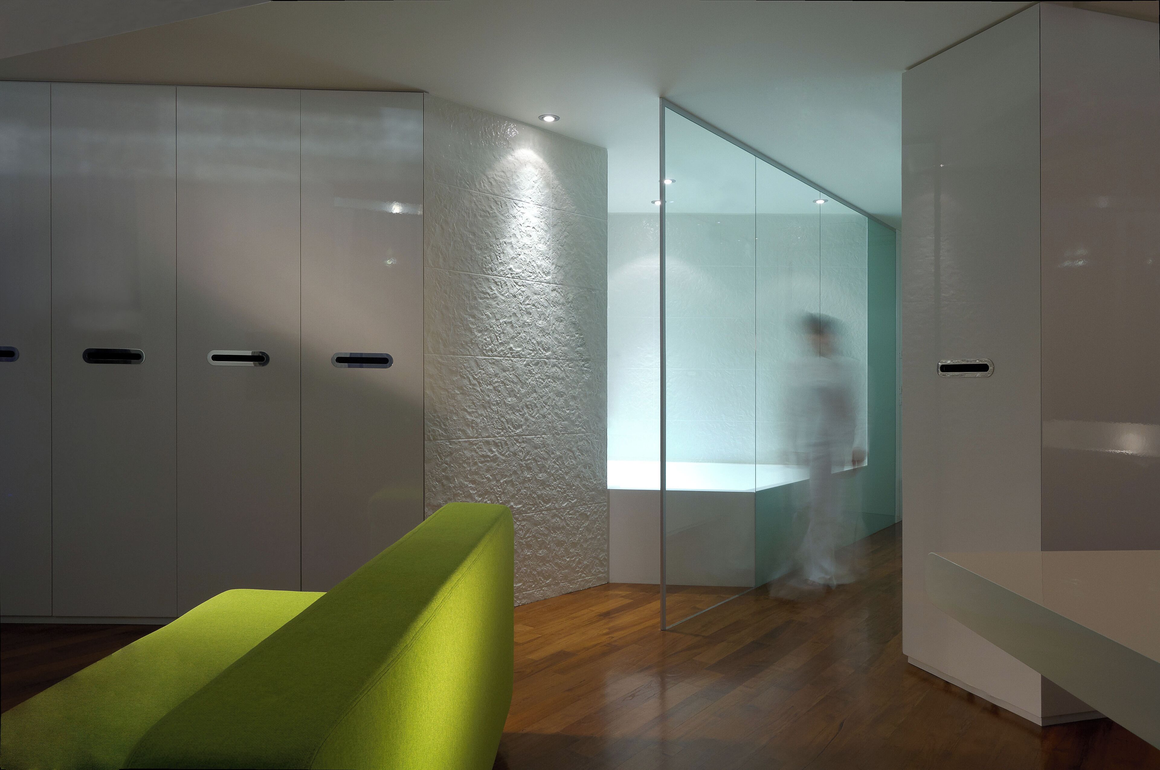 A modern interior with a wooden floor, a green chair, and a glass partition.