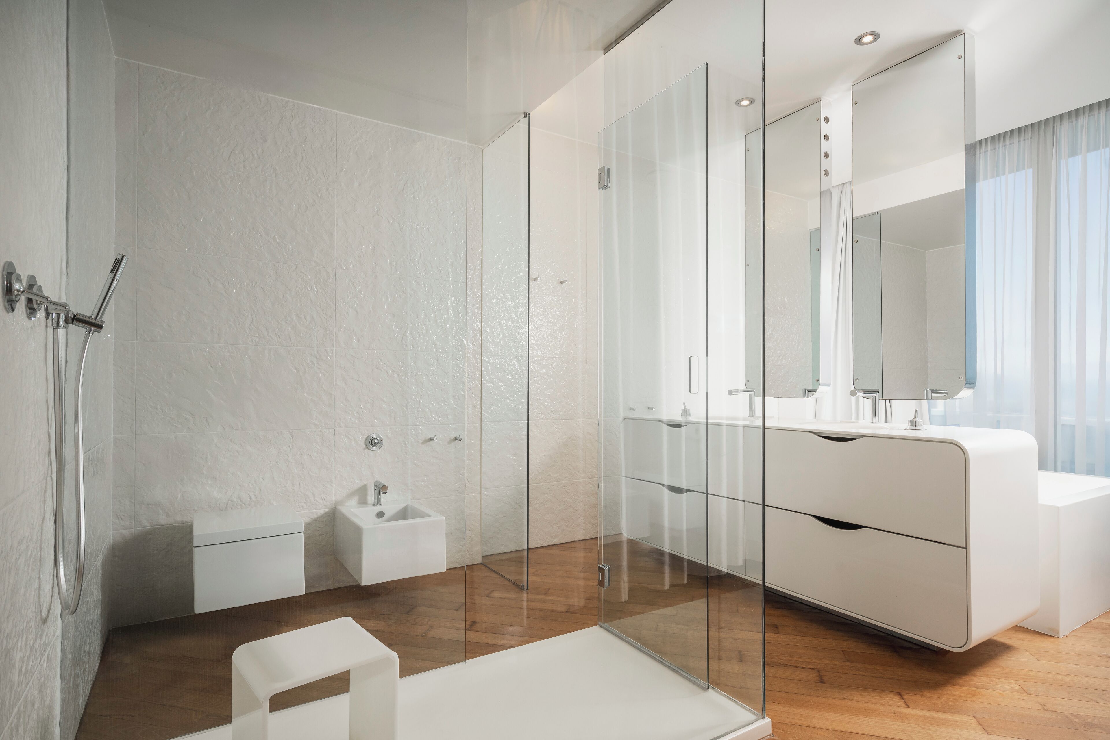 A modern bathroom with a glass shower enclosure, a white vanity with a mirror, and a wooden floor.