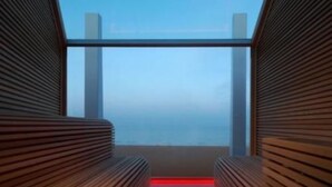 A corridor with wooden slats and a view of the sea through a large window.