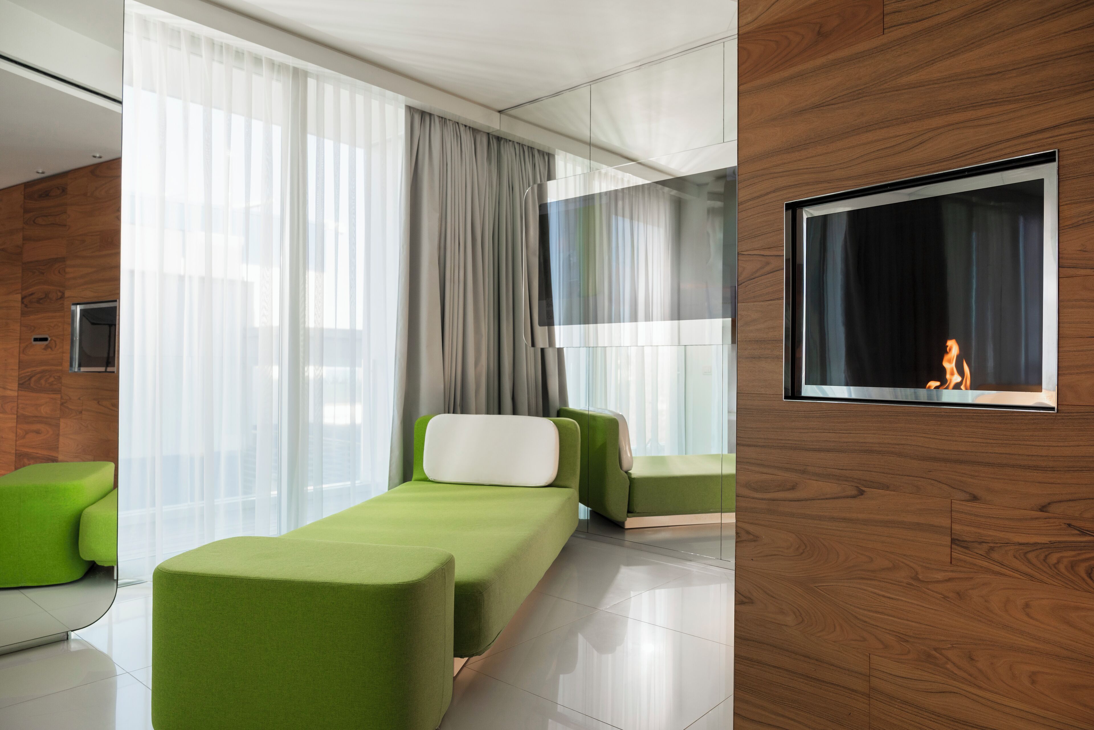 Ein modernes Hotelzimmer mit großem Fenster, Flachbildfernseher und grünen Polstermöbeln.