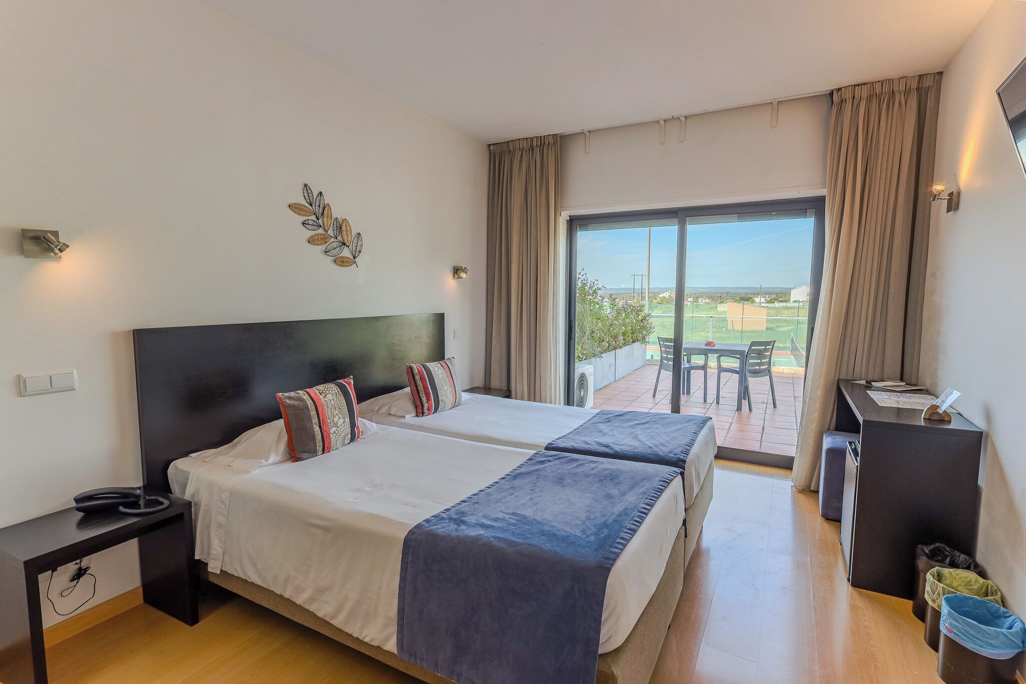 Une chambre d’hôtel avec deux lits, un balcon avec une table et des chaises, et un bureau avec une chaise.