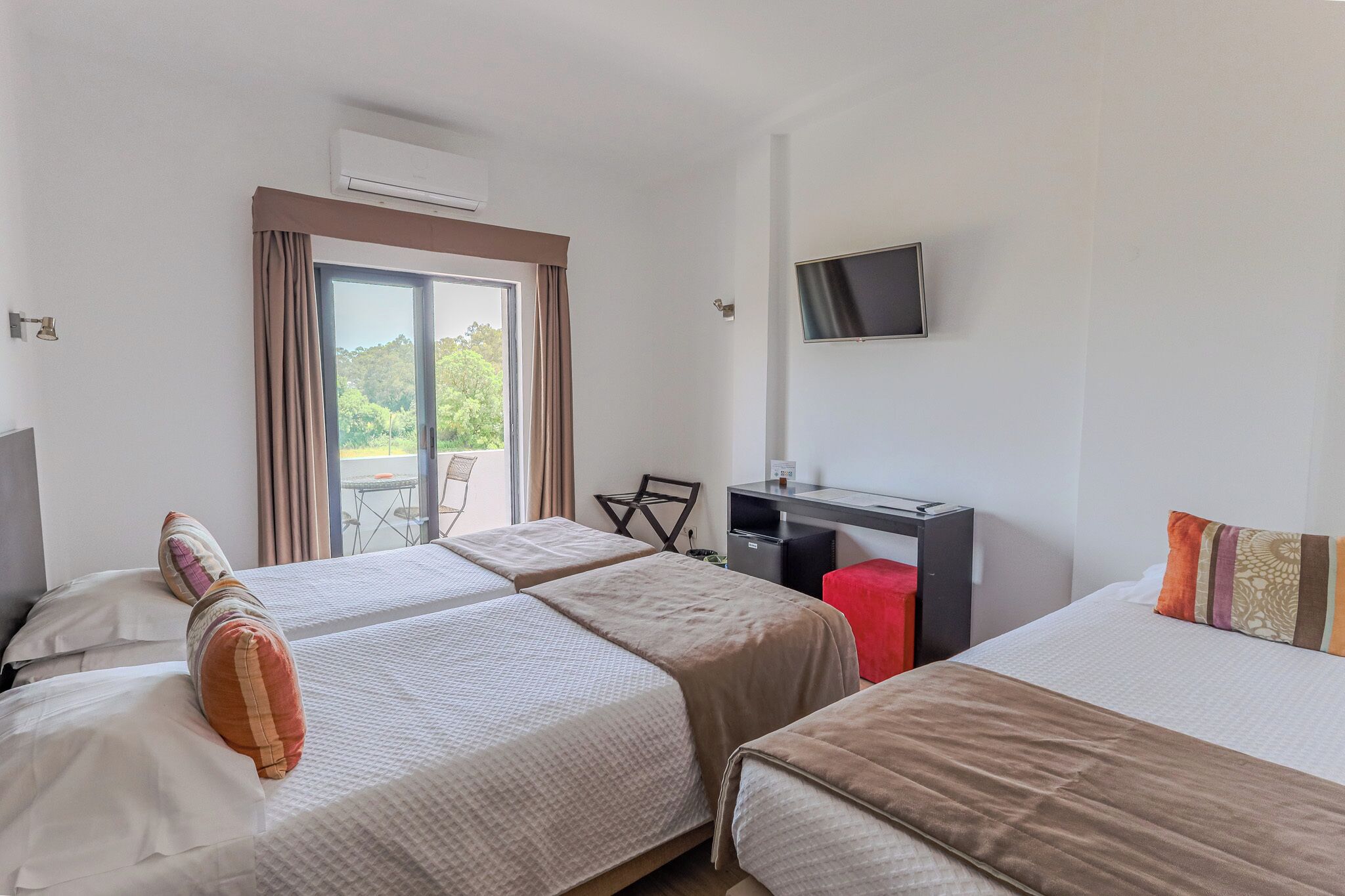 Une chambre d’hôtel avec deux lits, un bureau, une télévision et un balcon avec des rideaux.