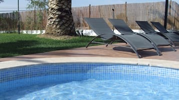 A swimming pool with tiled edges, surrounded by a grassy area and a palm tree.