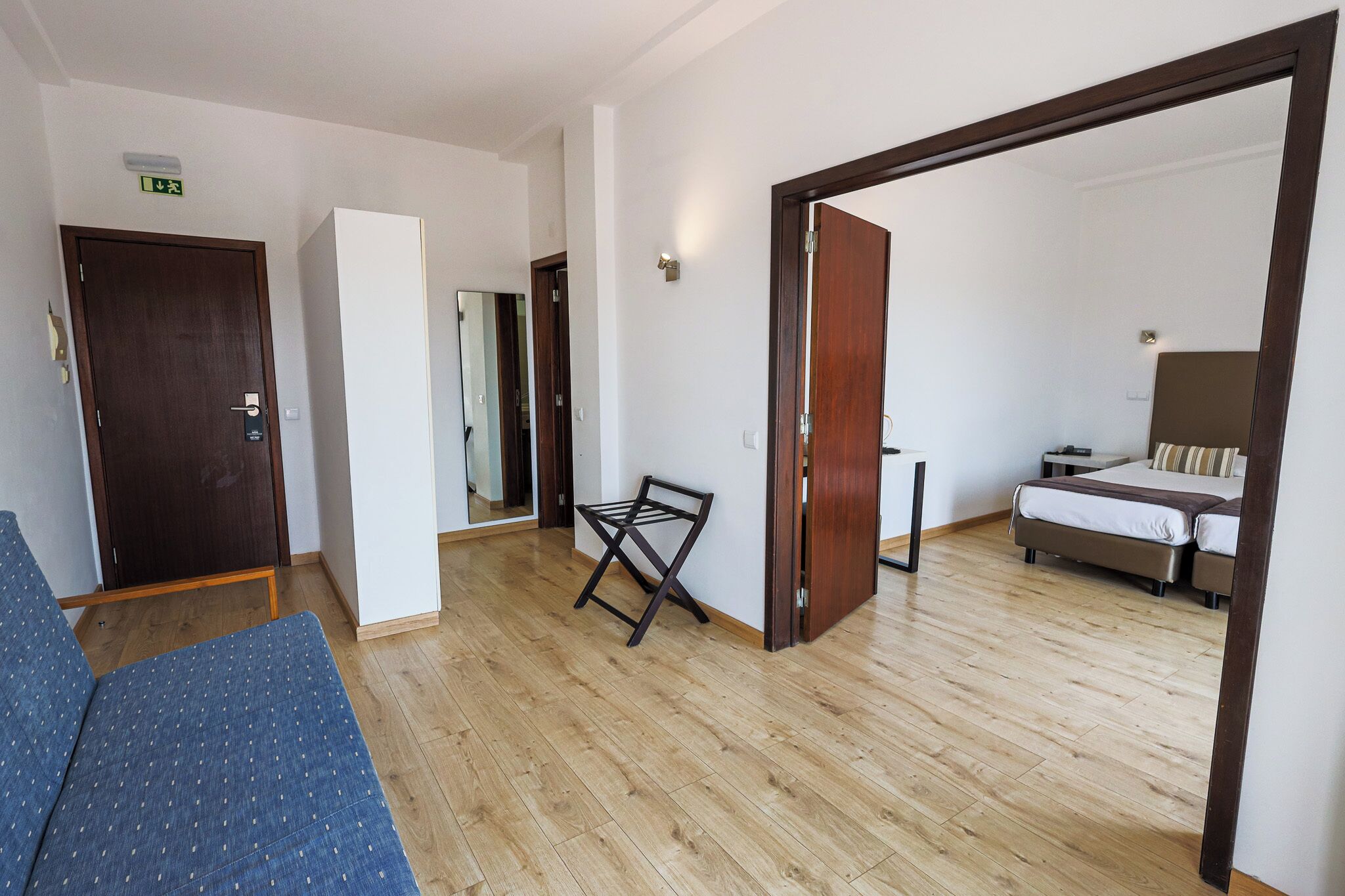 Una habitación de hotel con piso de madera, una cama, un sofá y una puerta que da a otra habitación.